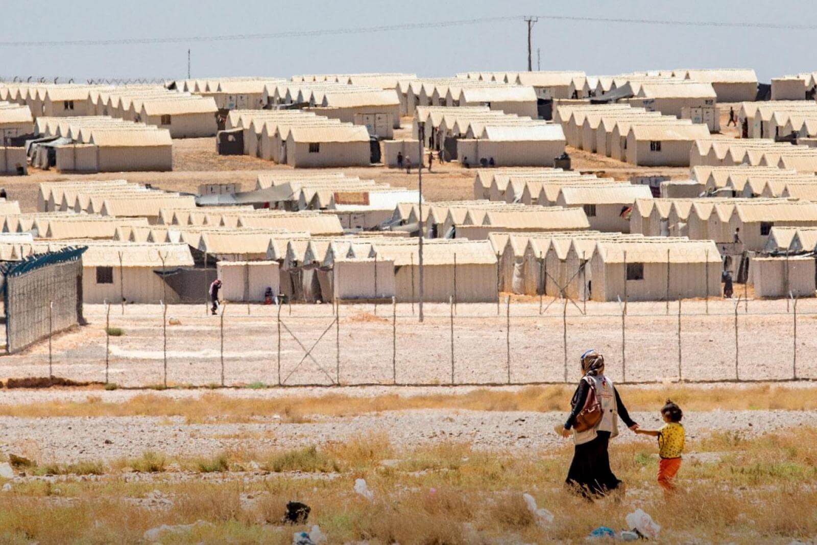 Mother and child walk hand in hand outside refugee camp.