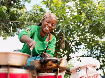 Woman smiling, cooking outside.