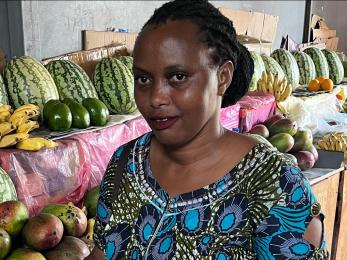 Woman stands smiling, in front of table of fruit.